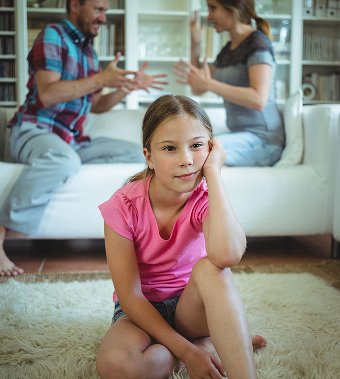 Child sitting on rug with adults arguing in the background, highlighting family tension and dynamics. Child sitting on rug with adults arguing in the background, highlighting family tension and dynamics.