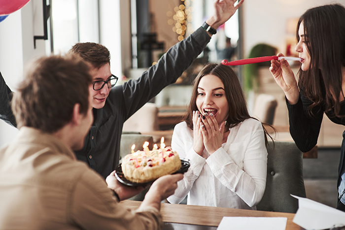 A woman surprised by a birthday cake celebration with friends, showcasing a lively setting. A woman surprised by a birthday cake celebration with friends, showcasing a lively setting.