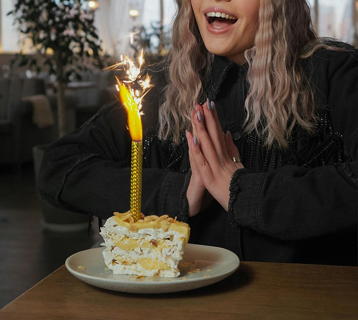 Woman anticipating grand birthday celebration with cake and sparkler, hands clasped. Woman anticipating grand birthday celebration with cake and sparkler, hands clasped.