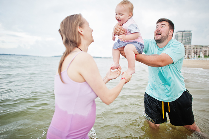 Family enjoying vacation at the beach, playing in the water with a baby.