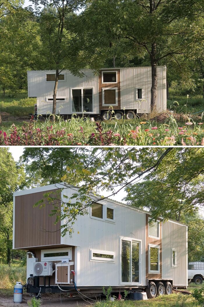 Tiny home nestled in a wooded area, featuring large windows and a modern design on a trailer.