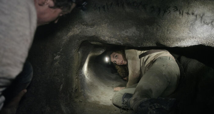 Person exploring a narrow cave passage, crouched and wearing a headlamp, symbolizing adventure over a cruise.