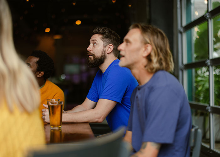 People sitting at a bar table, one holding a glass, engaged in conversation.