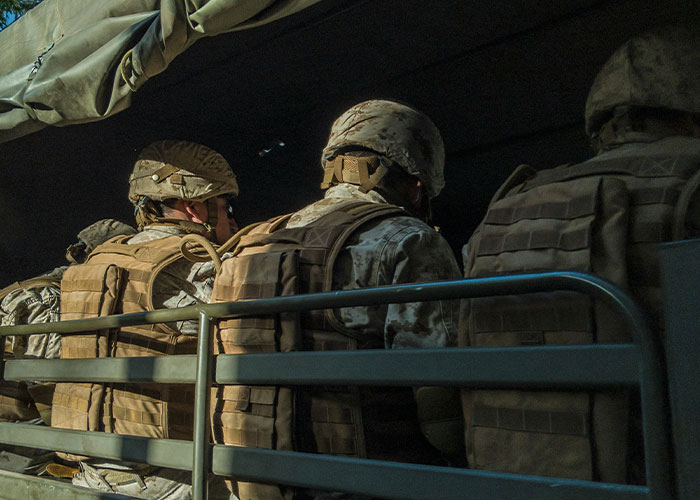 Soldiers in a military vehicle, wearing uniforms and helmets, with blurred faces, in a dimly lit setting.