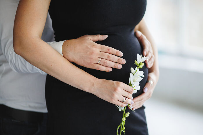 Pregnancy romanticized; close-up of hands on a pregnant belly, holding white flowers.