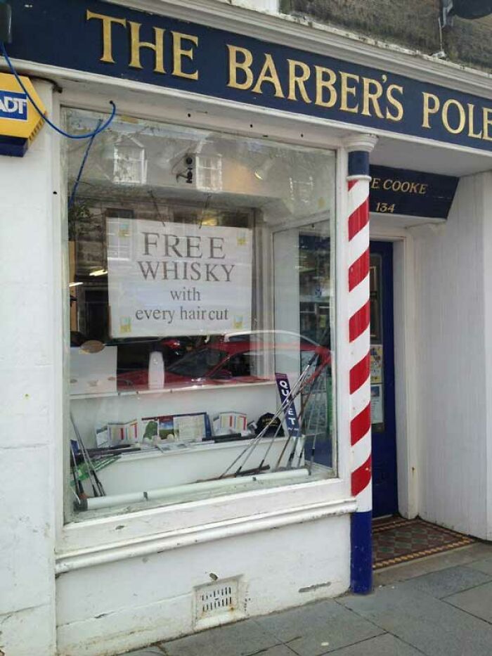 Barber shop window in Scotland offering free whisky with haircuts, highlighting local humor and culture.