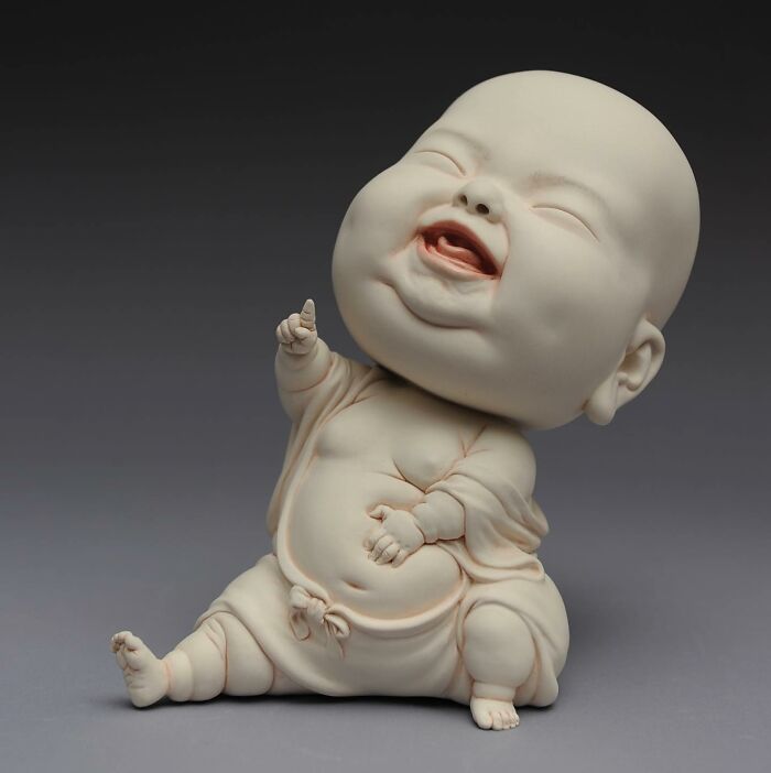 Sculpture blending realism and surrealism, depicting a joyful, large-headed baby figure in a seated pose.