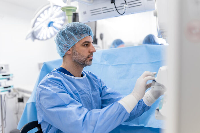 Surgeon in blue scrubs and cap, focused on equipment, representing a professional environment.
