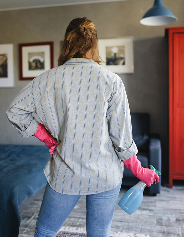 Person with cleaning supplies, wearing pink gloves, representing household chores.
