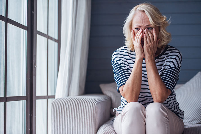 Woman in a striped shirt sitting on a couch, covering her face with her hands, looking distressed.