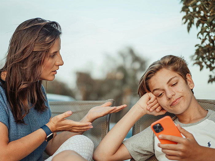 Woman talking to a teenage boy as he looks at his phone, highlighting views on chores and gender roles.