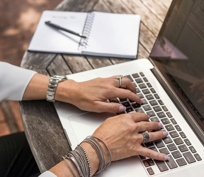 Hands typing on a laptop next to a notebook, illustrating online security measures.