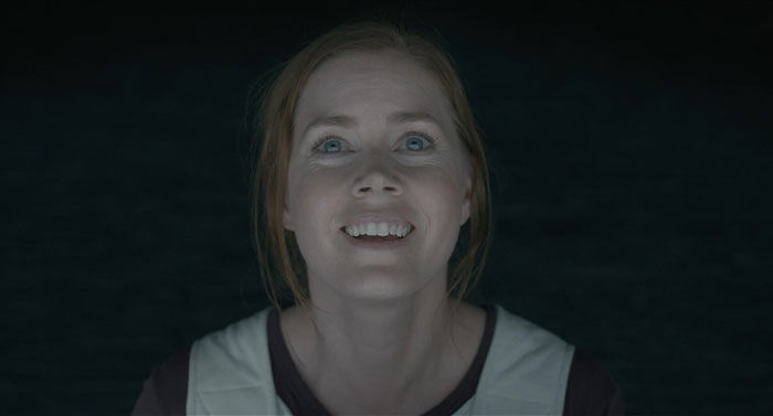 A woman with an engaging expression, representing a strong female protagonist in a dimly lit setting.