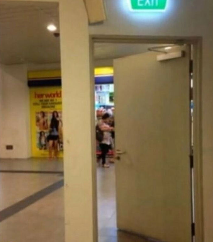 Exit door placed awkwardly, showcasing a construction fail, with a sign overhead and a misaligned angle towards the corridor.