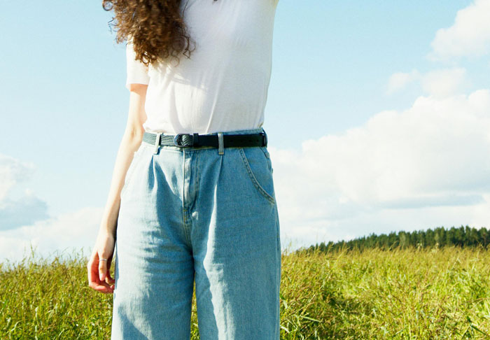 Person wearing high-waisted jeans and a white shirt in nature, showcasing a roasted fashion trend.