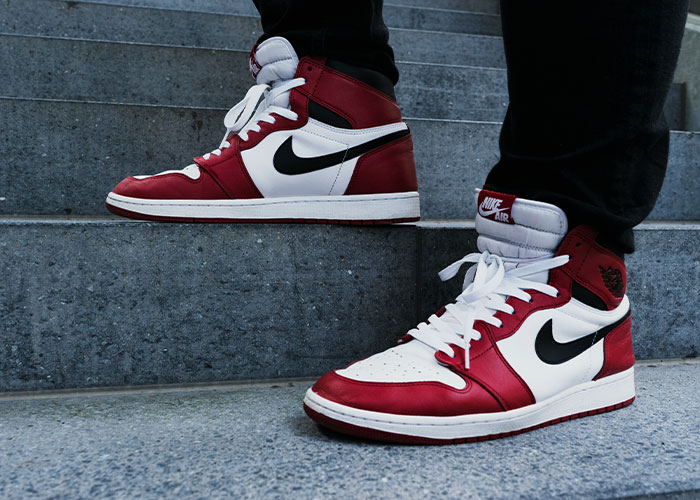 Red and white sneakers with a black logo worn by a person standing on a stone staircase.