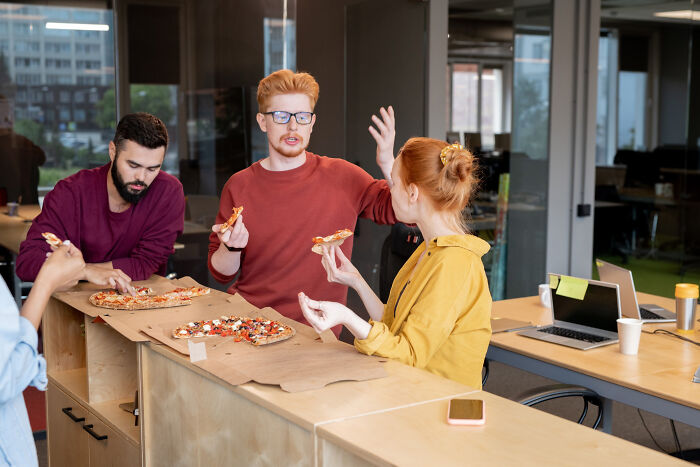 Office workers sharing pizza, discussing disappointing bonuses and benefits.