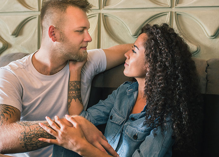 Couple sitting close on a sofa, looking into each other's eyes, sharing secrets.