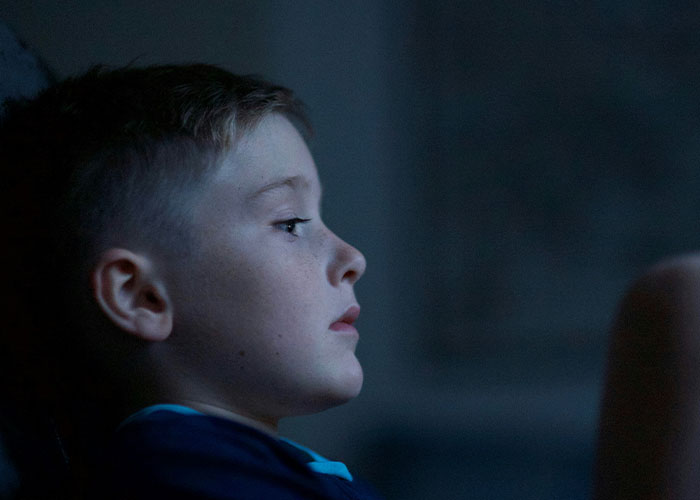 A child sitting in a dimly lit room, gazing thoughtfully off-camera.