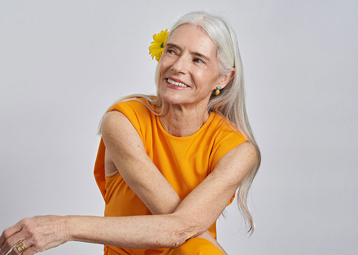 Woman in an orange dress, smiling with a flower in her hair, symbolizing secrets shared.