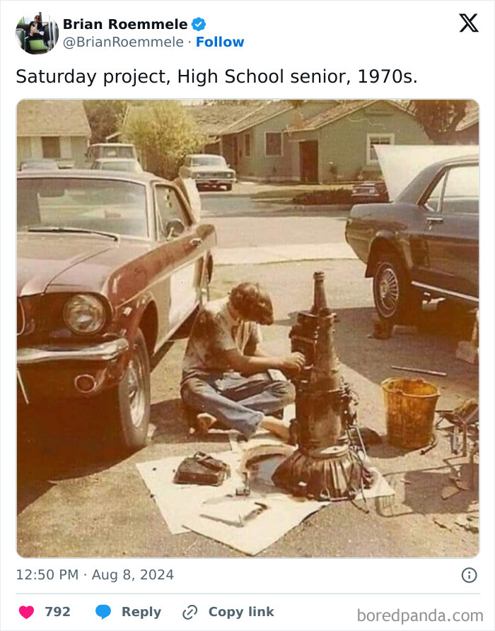 High school senior in the 1970s working on a car part outdoors next to vintage vehicles.
