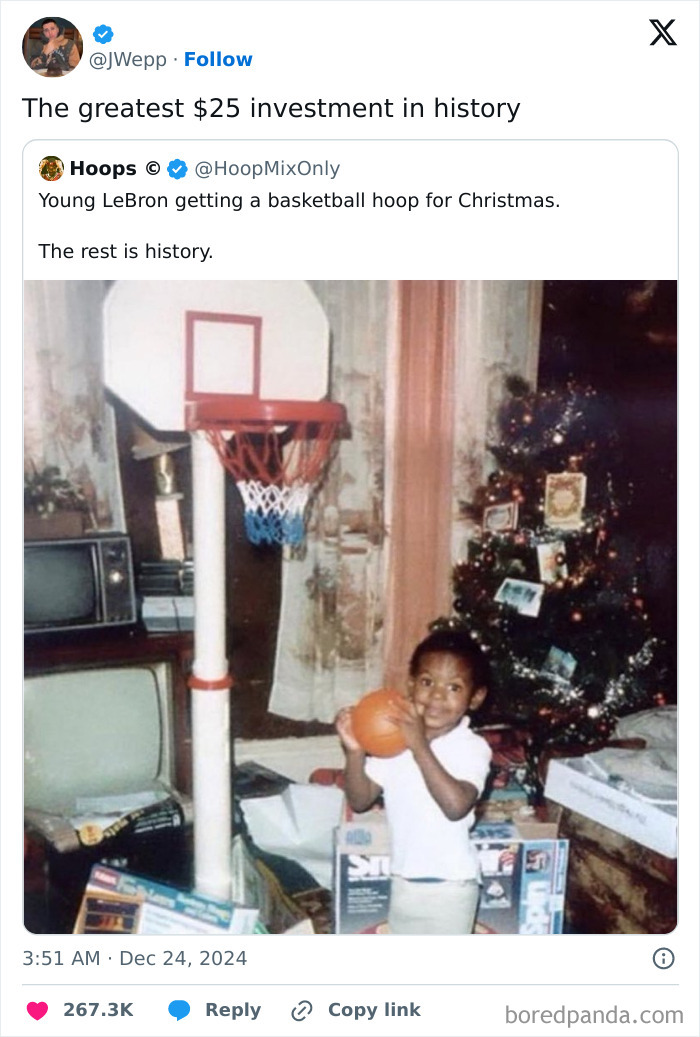 Young child holding a basketball next to a hoop by a Christmas tree.