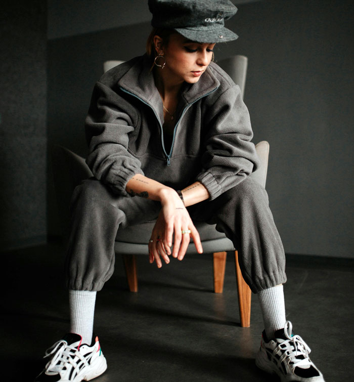 Person wearing a grey tracksuit, seated thoughtfully, exemplifying fashion trends some may dislike.