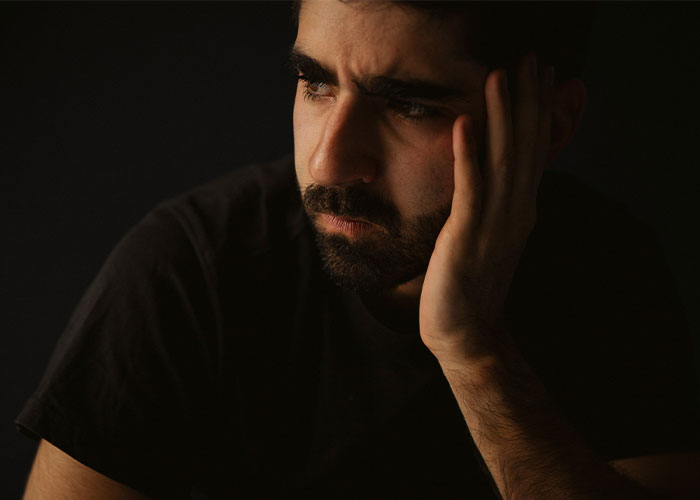 A contemplative man in a dark setting, reflecting deeply on drunk people spilling secrets.