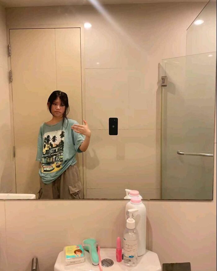 Person in a bathroom mirror, posing with hand gestures, wearing a tropical print shirt, resembling a potential album cover.