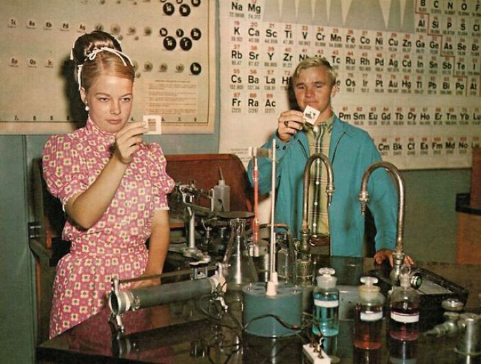 1970s high school science students conduct experiments in a chemistry lab, surrounded by equipment and a periodic table.