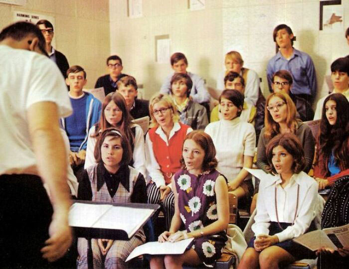 '70s high school choir practice with students in retro outfits, singing with focus and enthusiasm.