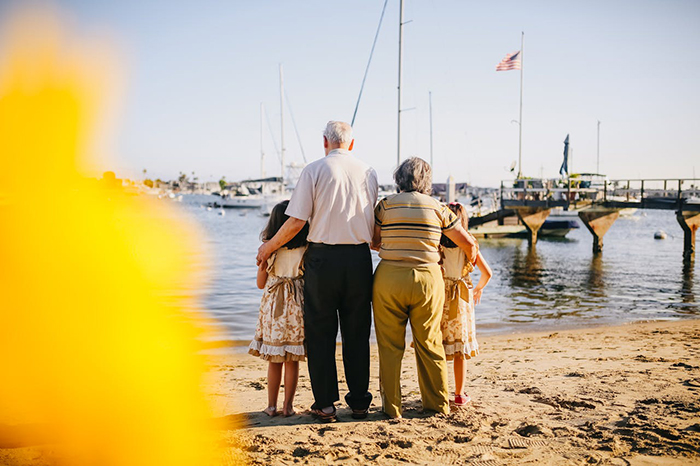 Elderly couple and children facing the ocean during an unexpected family vacation gathering.