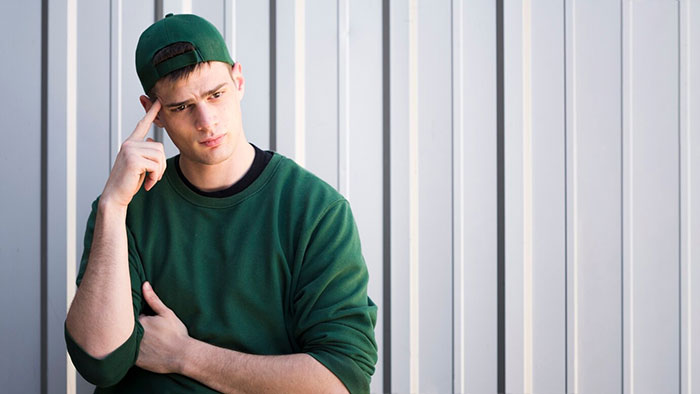 Teen brother in green sweater and cap, looking thoughtful against a metal wall. Teen brother in green sweater and cap, looking thoughtful against a metal wall.