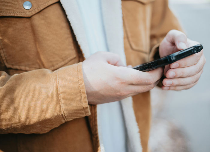 Person in a brown jacket using a smartphone outdoors, focusing on a texting activity. Person in a brown jacket using a smartphone outdoors, focusing on a texting activity.