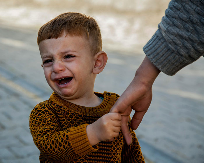A crying child in a brown sweater holds a parent's hand, symbolizing a temperamental moment. A crying child in a brown sweater holds a parent's hand, symbolizing a temperamental moment.