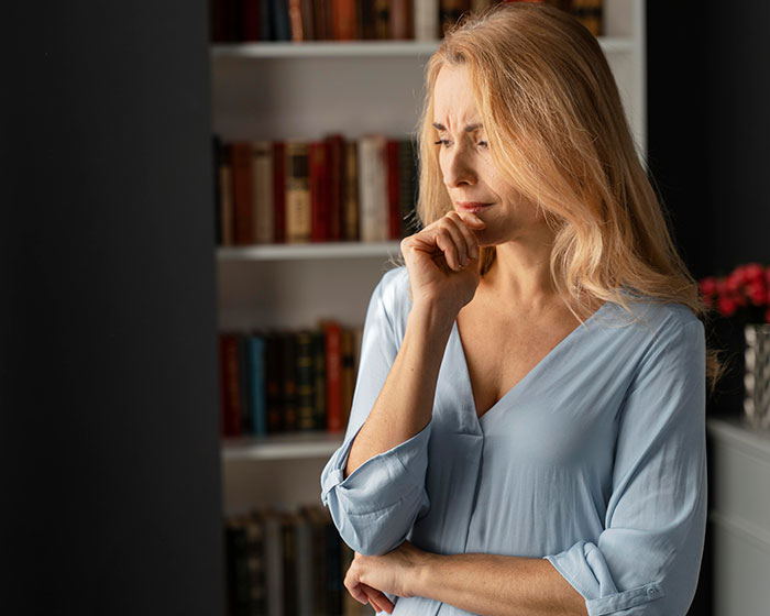 Woman in a light blue shirt looking concerned, standing in front of a bookshelf.