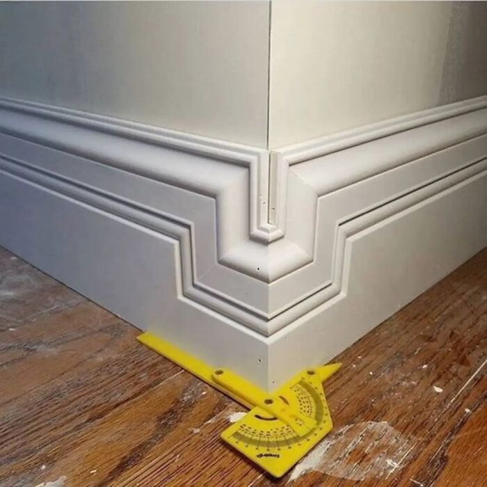 Misaligned baseboard corner showing funny cheap construction fail with a measuring tool on a wooden floor.