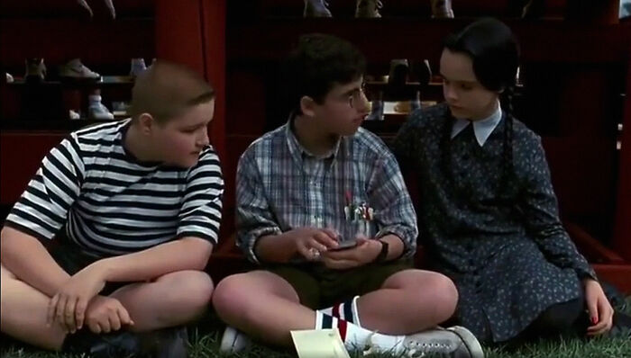 Children sitting on grass, possibly discussing movie jokes, wearing casual outfits and appearing engaged in conversation.