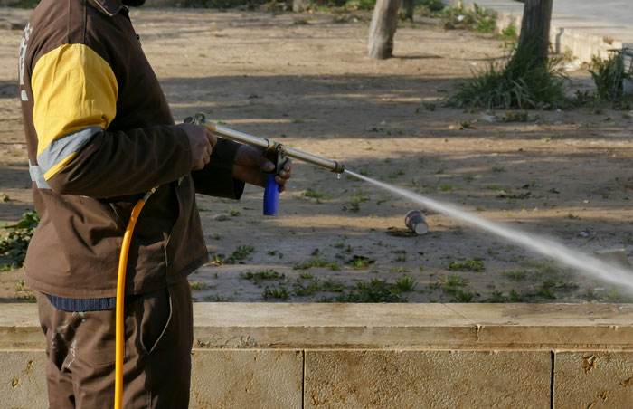 Person wearing work uniform using a hose in a park, potentially unsafe situation related to firing reasons.