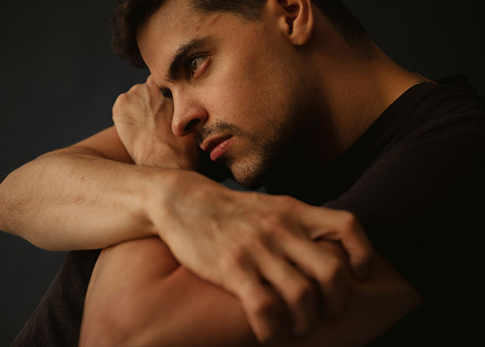 Pensive man sitting in a dark room, contemplating secrets and regrets.