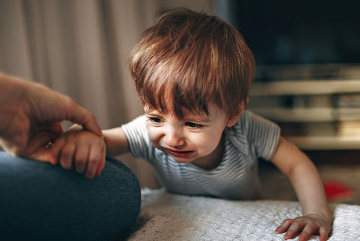 A toddler crying indoors, reaching for a person&rsquo;s hand, possibly related to a concussion.