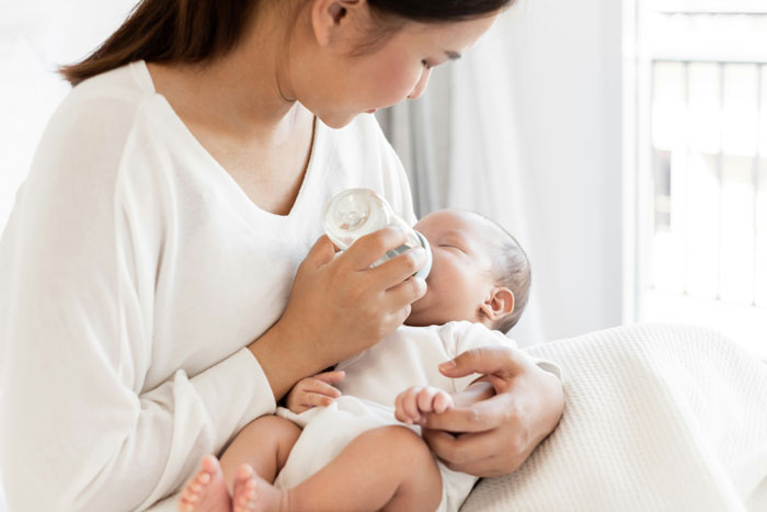 Woman feeding baby with formula milk in a cozy setting, highlighting concerns about its safety. Woman feeding baby with formula milk in a cozy setting, highlighting concerns about its safety.