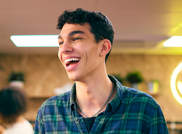 Teenager laughing in a warm-lit room, wearing a plaid shirt.