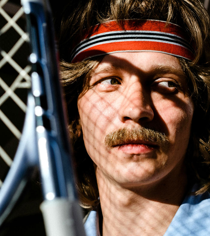 Person in a retro headband holding a tennis racket, shadowed by a fence, representing disliked fashion trends.
