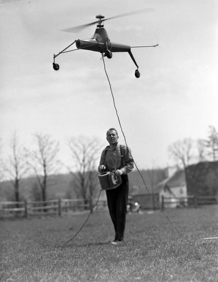 A man operates a vintage flying machine invention in an open field, showcasing early strange inventions.