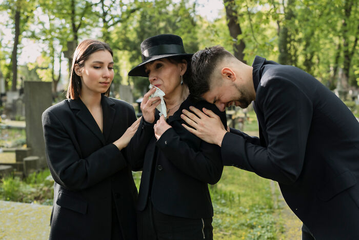 Three people in black clothing, comforting each other in a cemetery, conveying a sense of a terrible Christmas this year.