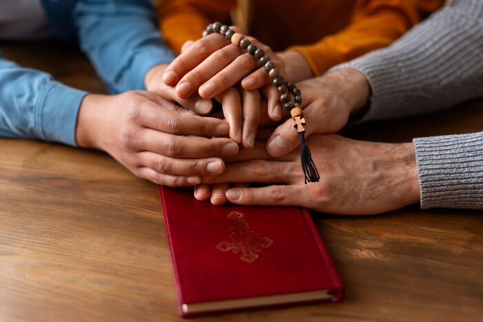 Hands holding rosary over a red book, symbolizing unity and contemplation of controversial takes.