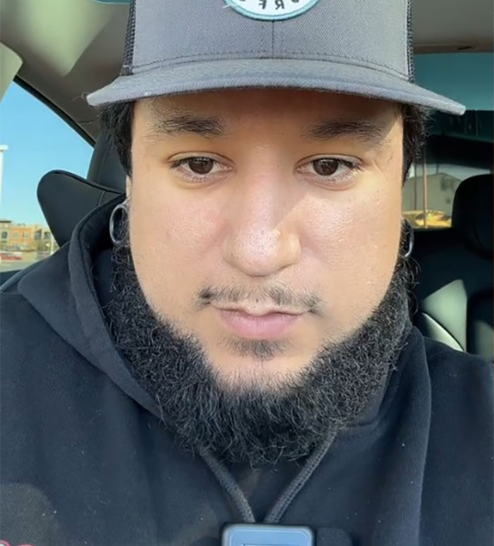 Person in a car wearing a black hoodie and cap, associated with viral post about dystopic retail games under capitalism. Person in a car wearing a black hoodie and cap, associated with viral post about dystopic retail games under capitalism.