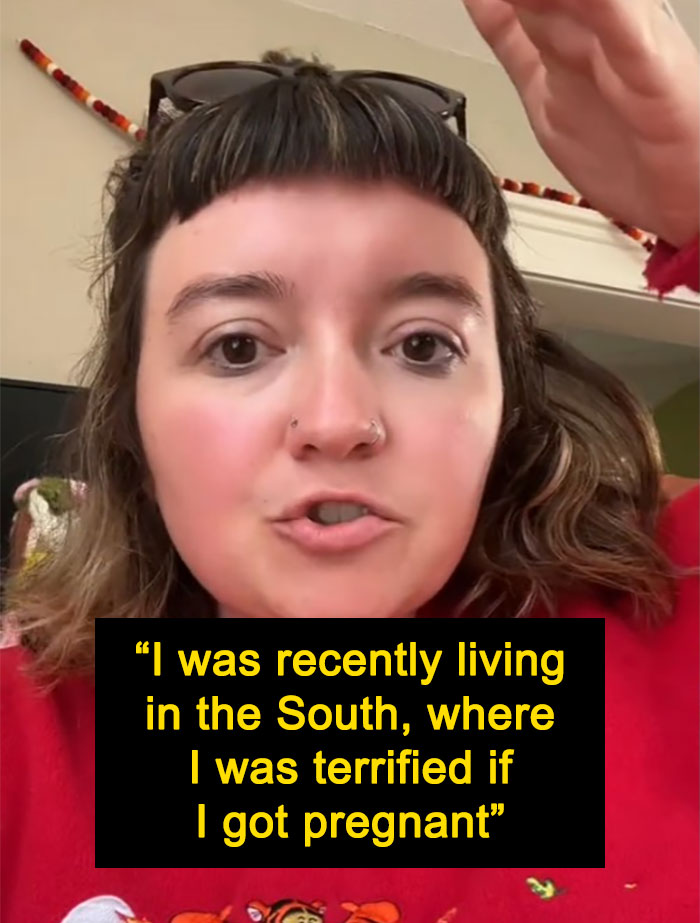 Woman sharing thoughts after moving to a blue state, wearing a red sweater and speaking in a room, expression thoughtful.