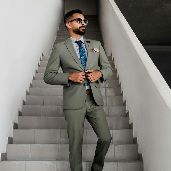 Man in a fashionable suit and sunglasses standing confidently on stairs, related to fashion trends.